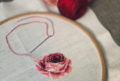 Handmade embroidery of a rose with needle and thread on fabric.